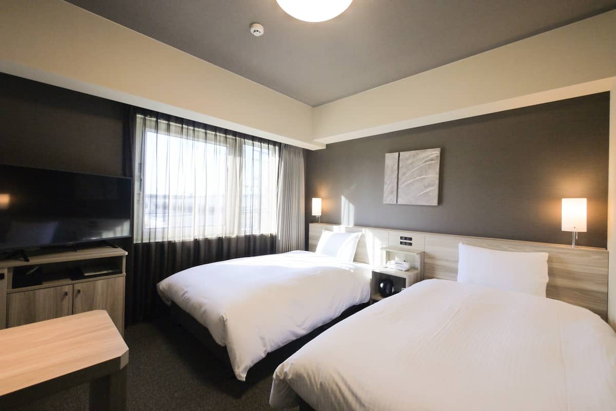Ein Hotelzimmer mit zwei Betten, einem Fernseher, einem Schreibtisch und einer Lampe.