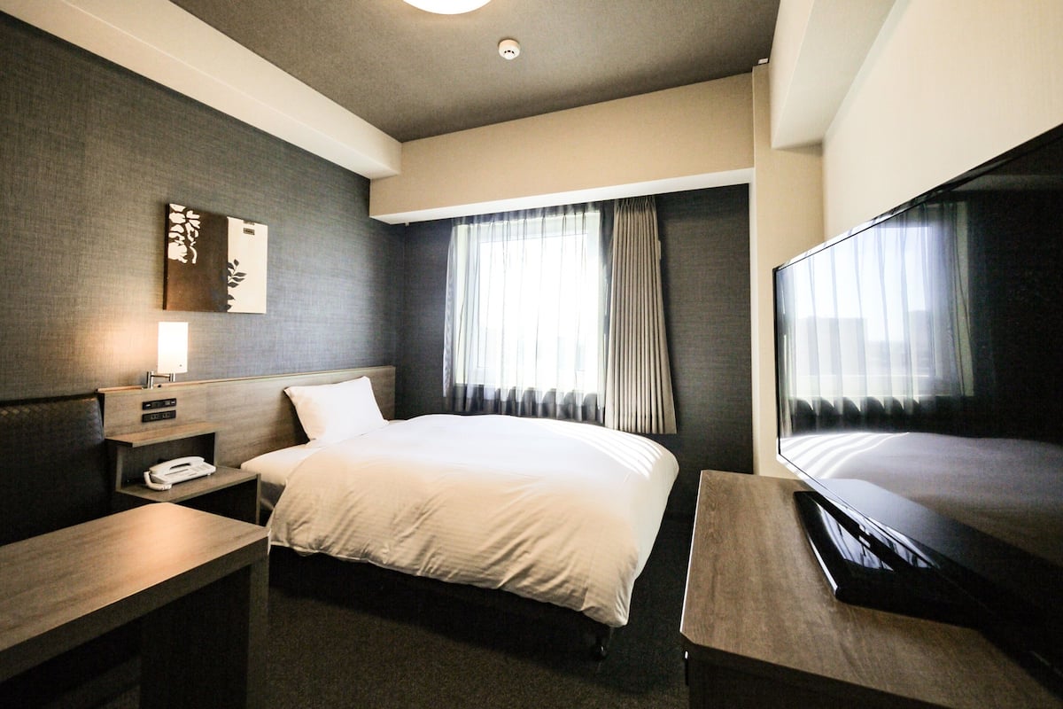 Ein Hotelzimmer mit Bett, Nachttisch, Lampe und Fernseher.