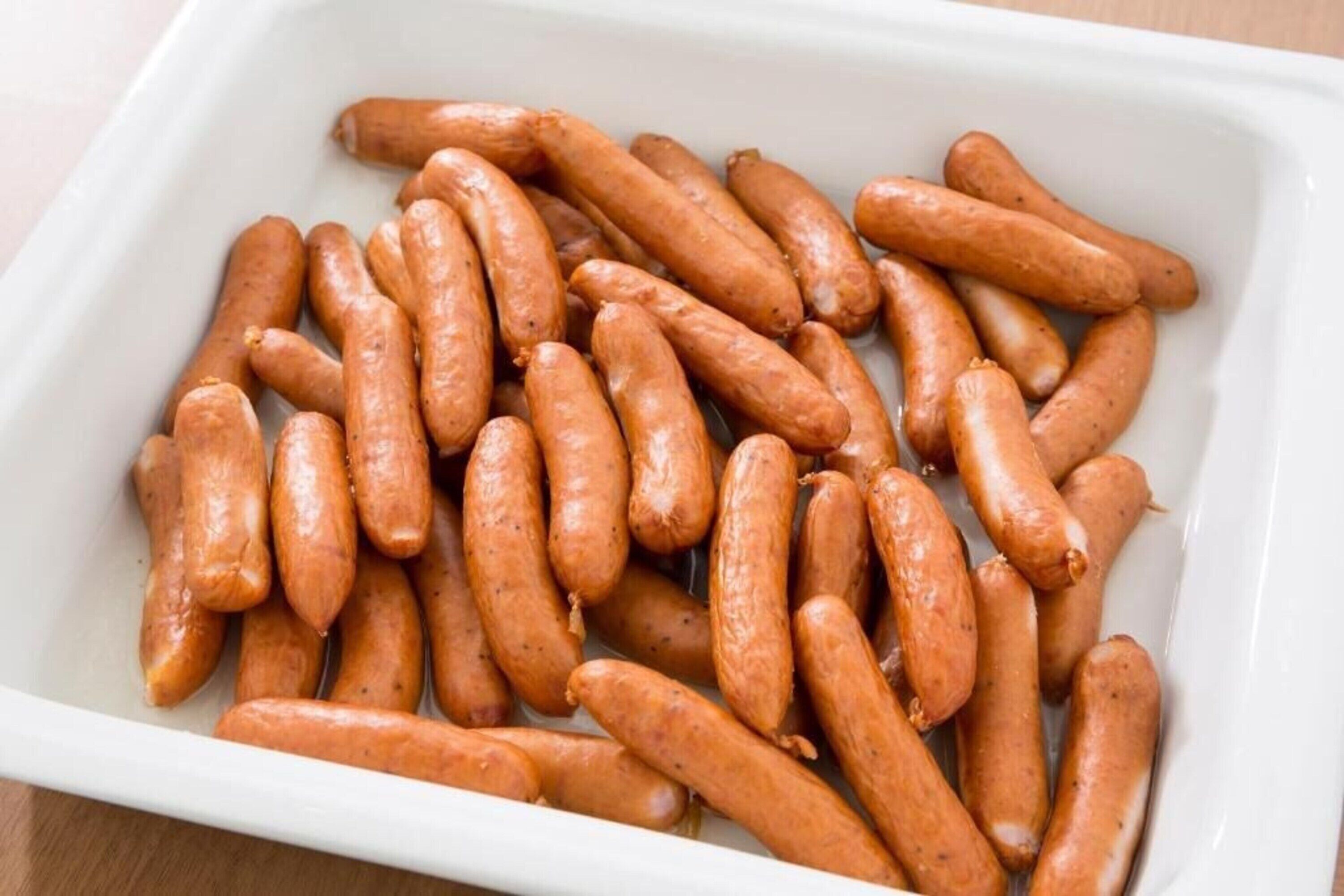 A white rectangular container filled with uncooked sausages.