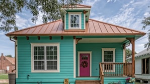 Una casa turquesa con puerta roja, un pequeño porche y techo de metal.