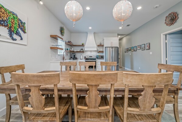Una cocina moderna con armarios blancos, un refrigerador de acero inoxidable y una amplia mesa de comedor con sillas de madera.