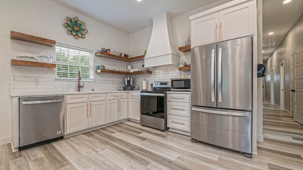 Una cocina moderna con armarios blancos, electrodomésticos de acero inoxidable y estantes de madera.