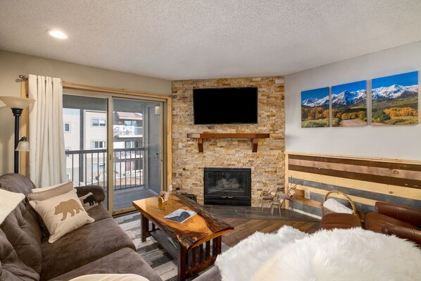 A cozy living room with a fireplace, a sofa, a coffee table, and a TV mounted on the wall.