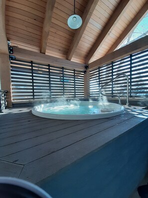 A hot tub in a wooden room with a sloped ceiling and large windows.