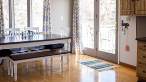 Un comedor con una mesa y bancos de madera, una cocina con armarios de madera, y vistas a través de un ventanal.