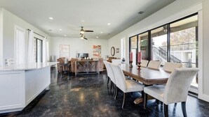 Una cocina amplia con una isla central, un comedor con una mesa grande y sillas, y vistas al exterior a través de amplios ventanales.