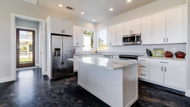 Una cocina moderna con armarios blancos, una isla central, electrodomésticos de acero inoxidable y suelo de mármol negro.