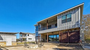 Una casa moderna de dos pisos con balcón, garaje y un patio con mobiliario exterior.
