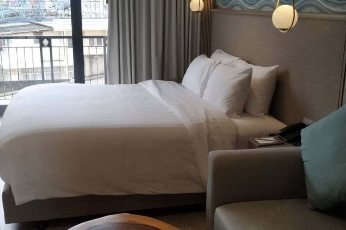 A hotel room with a large bed, a sofa, and a view of the cityscape through the window.