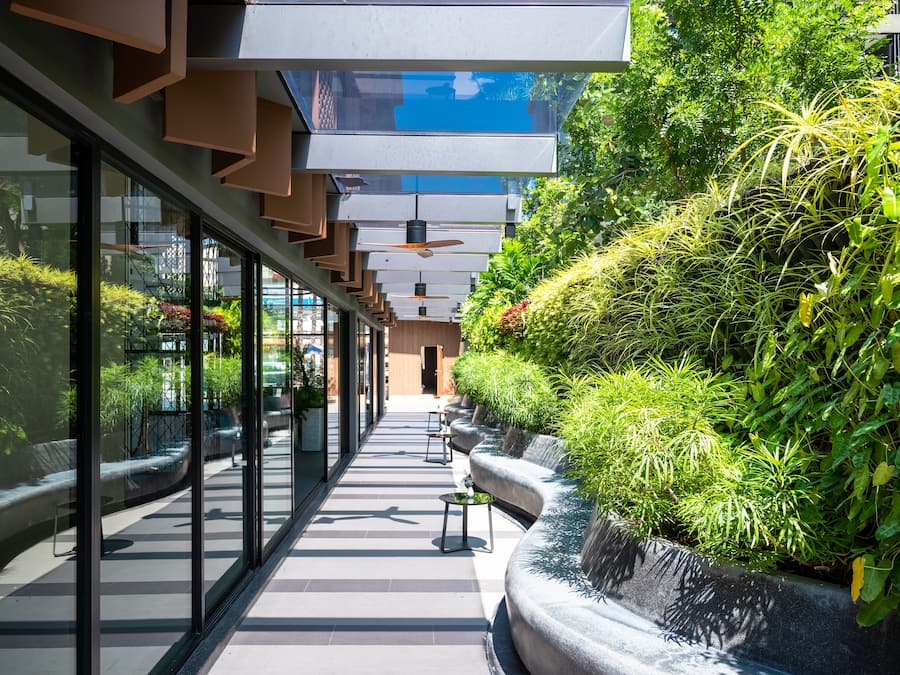 A modern corridor with glass walls, potted plants, and a bench.