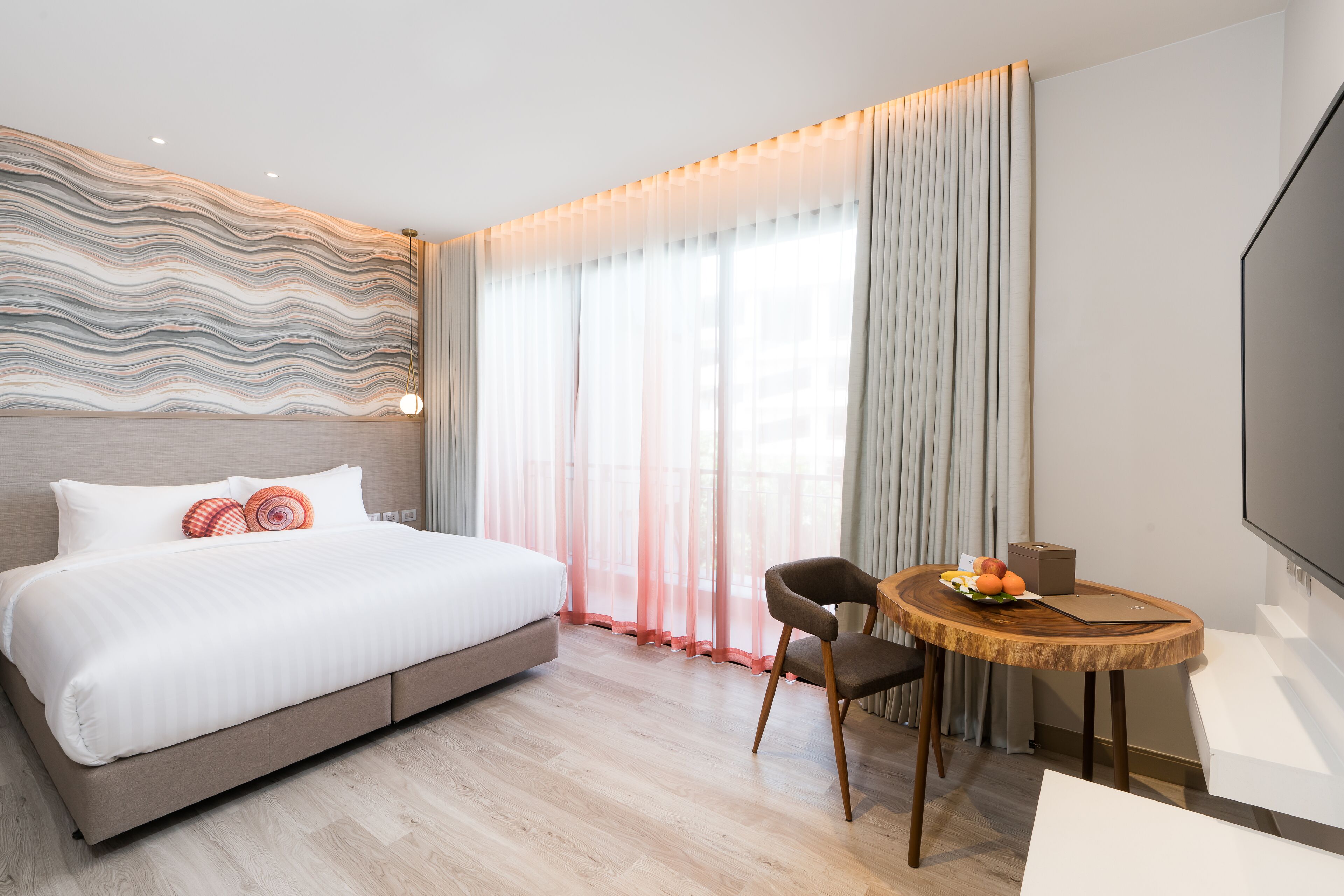 A modern hotel room with a large bed, a wooden dining table, and a flat-screen TV.