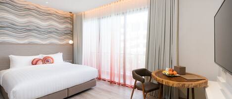 A modern hotel room with a large bed, a wooden dining table, and a flat-screen TV.