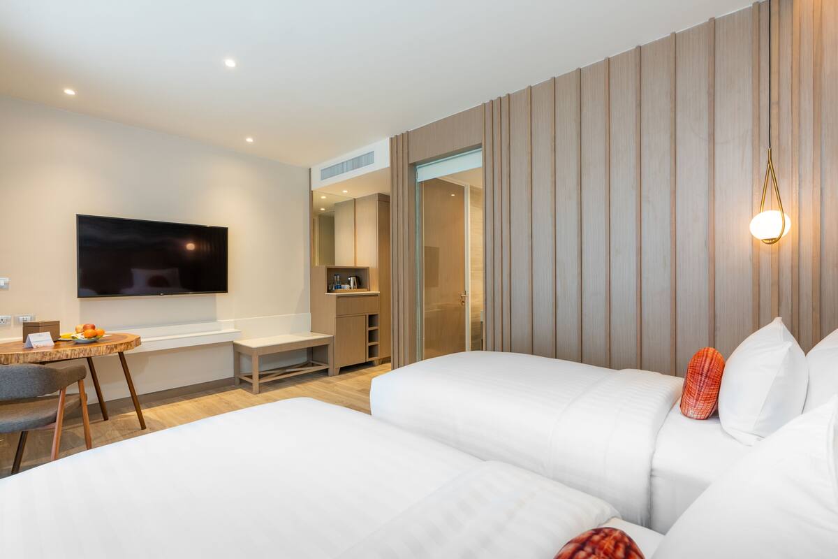 A modern hotel room with a flat-screen TV mounted on the wall, a desk with a chair, and a bed with white bedding.