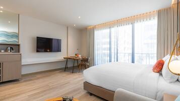 A modern hotel room with a large bed, a desk with a chair, a television mounted on the wall, and a balcony with curtains.