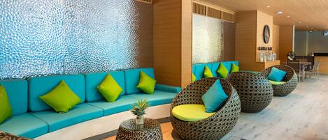 A modern lounge area with a blue sofa, wicker chairs, and patterned side tables.