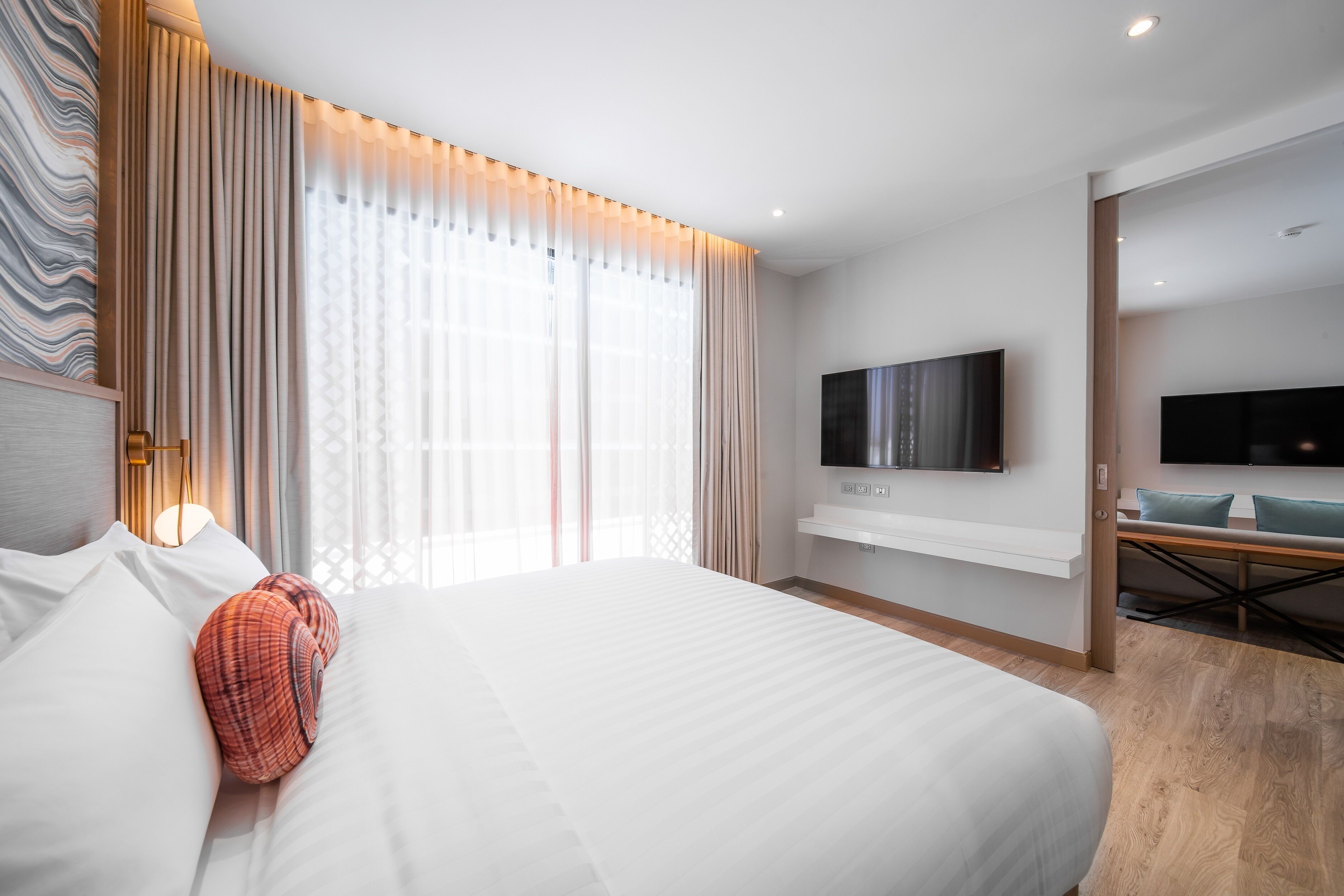 A modern hotel room with a large bed, a flat-screen TV mounted on the wall, and a seating area with a table and chairs.