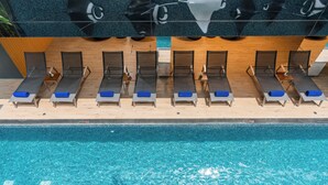 A poolside area with sun loungers aligned along the edge, a wooden deck, and a clear blue pool. - Maven Stylish Hotel Hua Hin (Hua Hin)