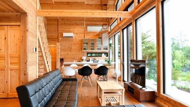 A modern log cabin interior with a sofa, dining table, and chairs, large windows, and a kitchen area. - Polar House Nishikaruizawa 1 (Karuizawa)