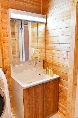 A wooden cabin bathroom with a white sink, mirror, and wooden cabinets. - Polar House Nishikaruizawa 1 (Karuizawa)