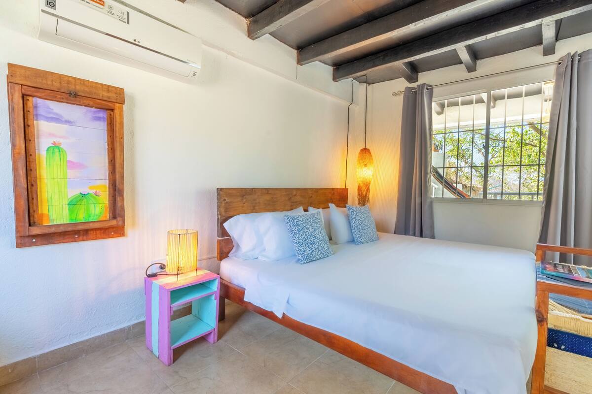 Un dormitorio con una cama de madera, una mesita de noche con lámpara, un estante colorido y un cuadro enmarcado.