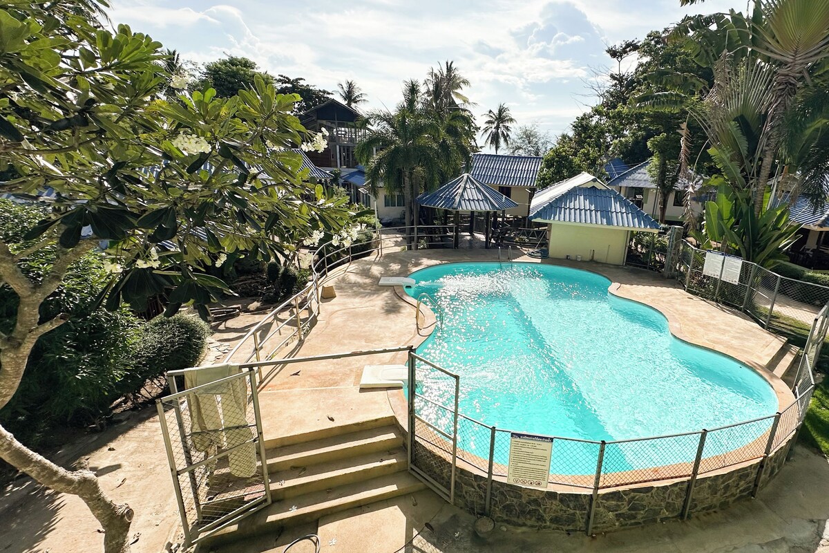 A swimming pool with a stone border, surrounded by a fence, and a staircase leading down to the pool.