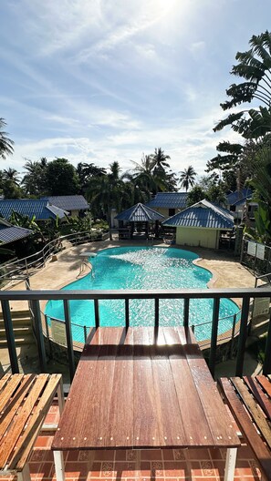A pool area with a wooden deck, surrounded by palm trees and covered structures. - Pranee Bungalow (Koh Tao)
