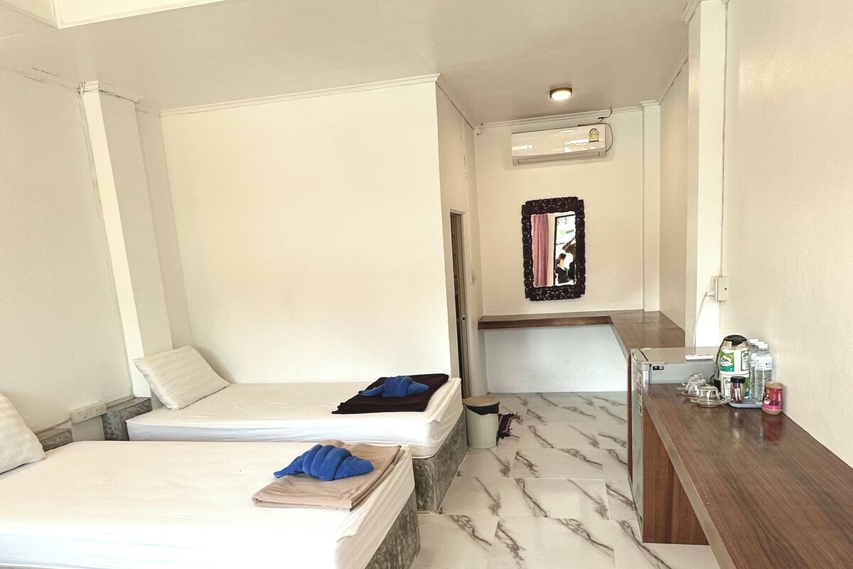 A hotel room with two beds, a marble-patterned floor, a wooden bench, and a small table with items on it.