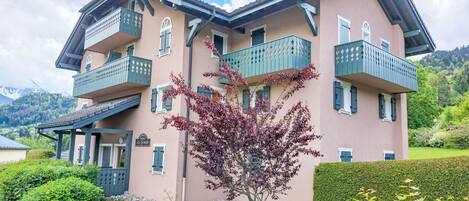 A multi-story building with balconies, a sign reading "Le Genova," and a garden with a tree in the foreground.