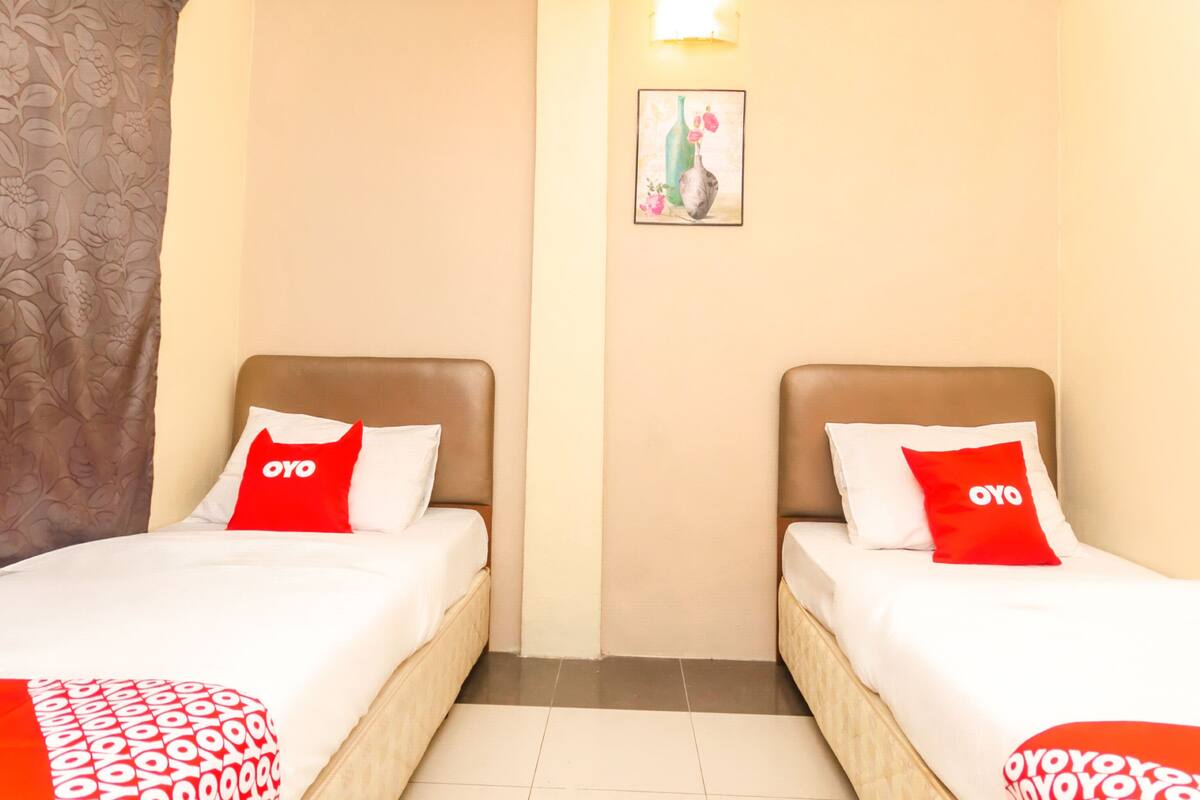 Een hotelkamer met twee bedden, elk voorzien van een rood kussen en een wit sprei.