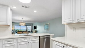 A modern kitchen with white cabinetry, a stainless steel dishwasher, and a large island with seating. - Oceanfront | Pool View | Gorgeously Furnished 3rd Floor Amelia Surf and Racquet Condo (Fernandina Beach)