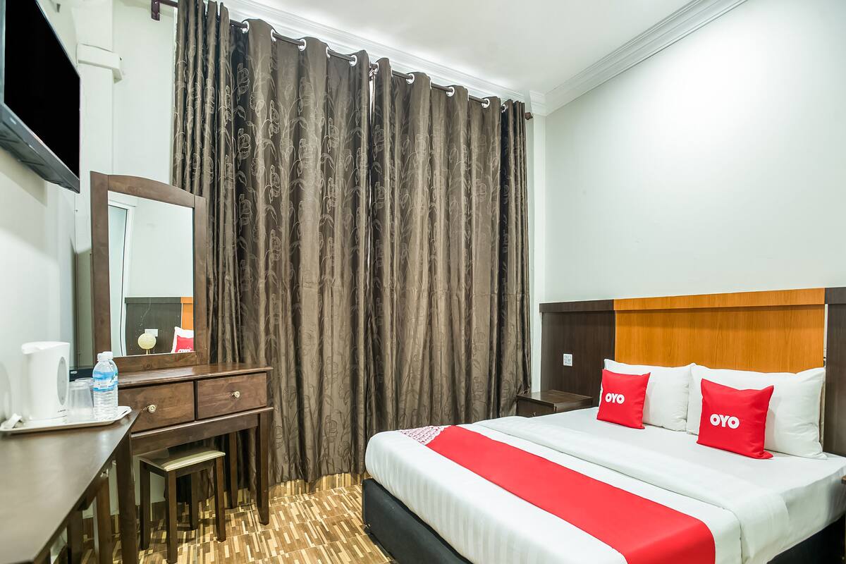 A hotel room with a bed, a desk, a mirror, and a window with curtains.