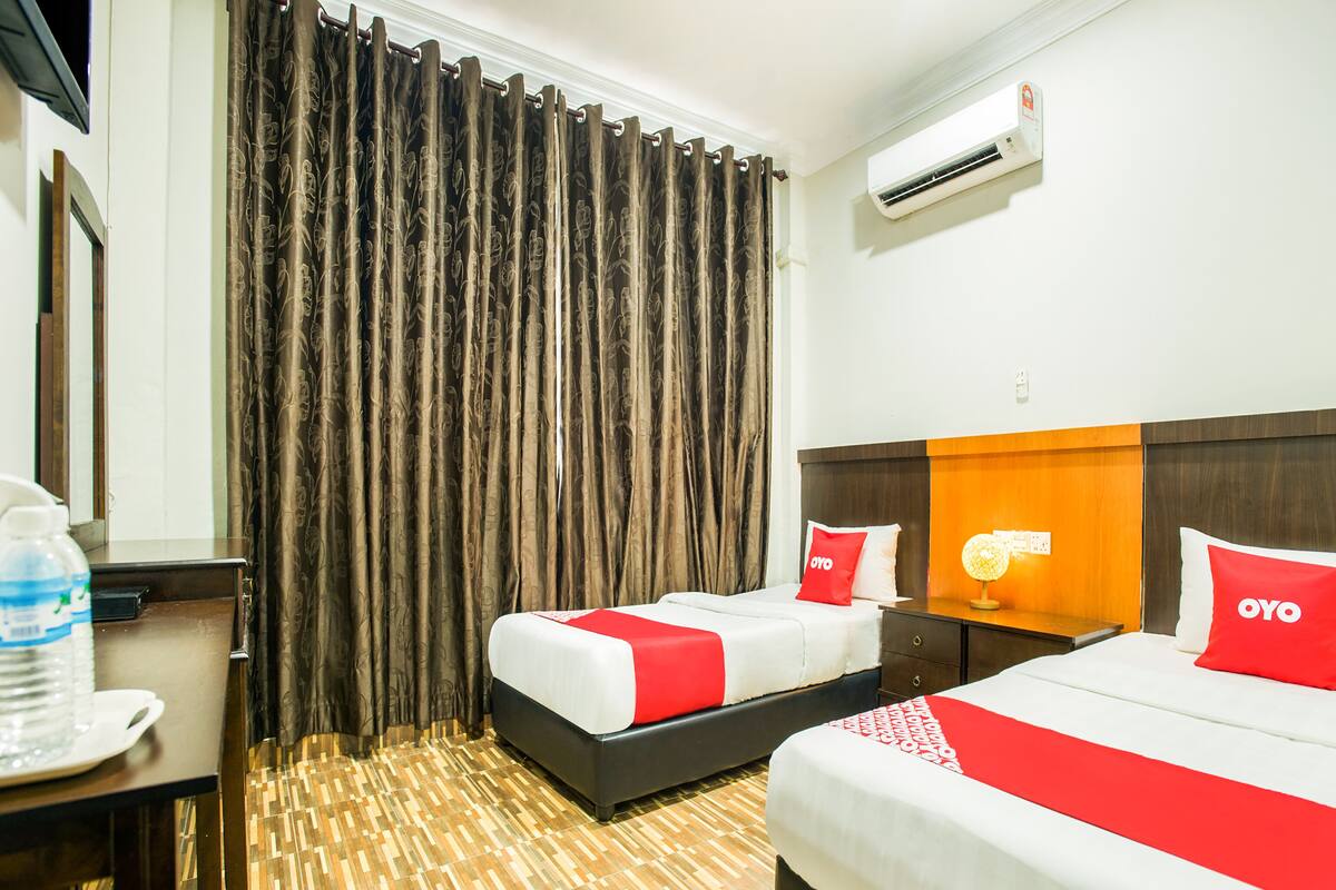 A hotel room with two beds, a desk, and a water bottle.