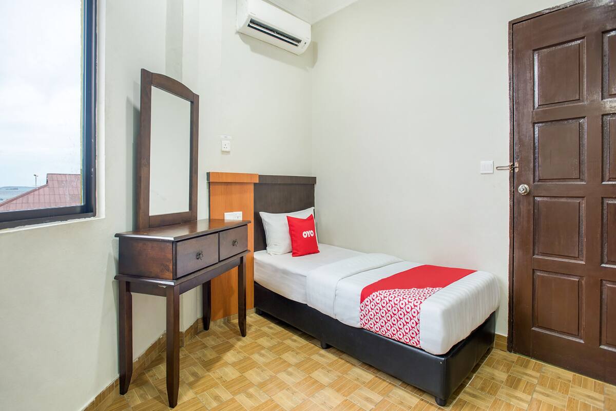 A hotel room with a bed, a dresser, a mirror, an air conditioning unit, and a wooden door.