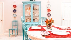 Un comedor con una mesa redonda para cuatro, un aparador azul con puertas de cristal y un reloj de pared.