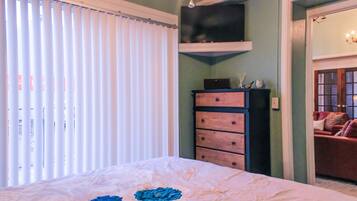 A bedroom with a bed, a dresser, a television on a shelf, and a door leading to another room.