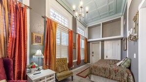 Un dormitorio con cama, una silla, una mesita de noche y un ventanal con cortinas.