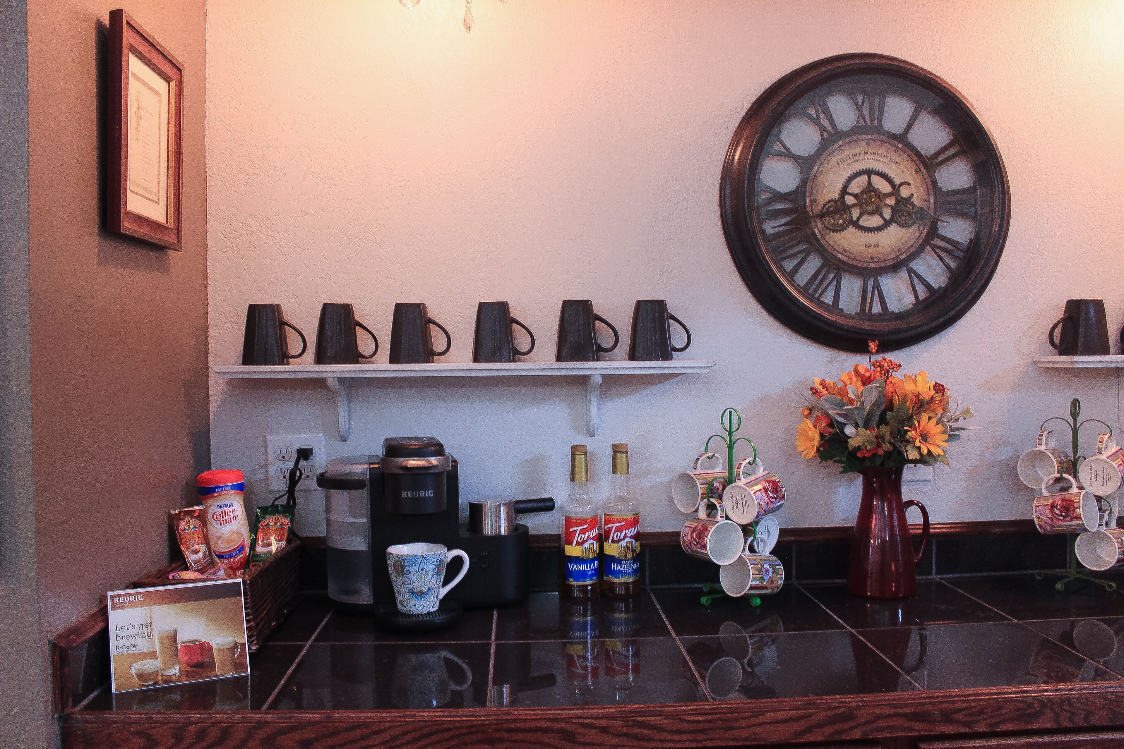 A kitchen counter with a coffee maker, mugs, and a clock.