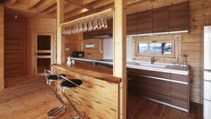 Un intérieur en bois comprenant un espace cuisine avec un ensemble de tabourets de bar, une fenêtre et des armoires en bois.