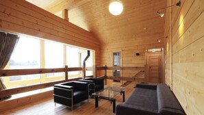 L’intérieur d’un chalet en bois, avec un canapé, une table en verre et une grande fenêtre.