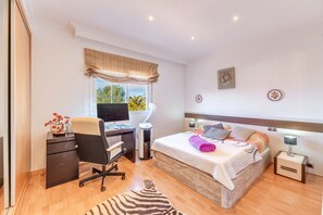 A bedroom with a bed, desk, chair, and a window with curtains.