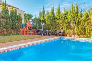 A swimming pool with a tiled edge, surrounded by greenery and a barbecue area.