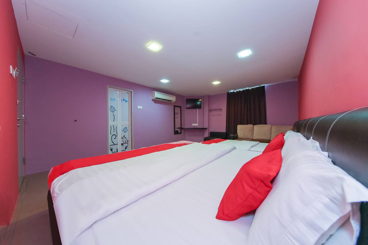 A hotel room with a bed, a chair, and an air conditioning unit.