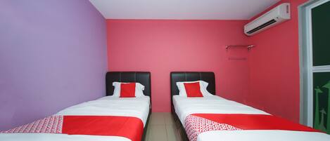 A room with two beds, each with a red and white bedspread, against a pink wall.