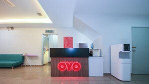 Un espace d’accueil avec un comptoir de réception portant l’inscription « OYO », un distributeur d’eau, un canapé vert et un panneau indiquant « KELUAR 2 ».