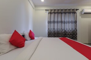 Ein Hotelzimmer mit einem Bett, roten Kissen, einem gemusterten Vorhang und einer Klimaanlage.