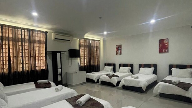 Habitación de hotel con cuatro camas individuales, un televisor de pantalla plana, un equipo de aire acondicionado y cortinas en las ventanas.