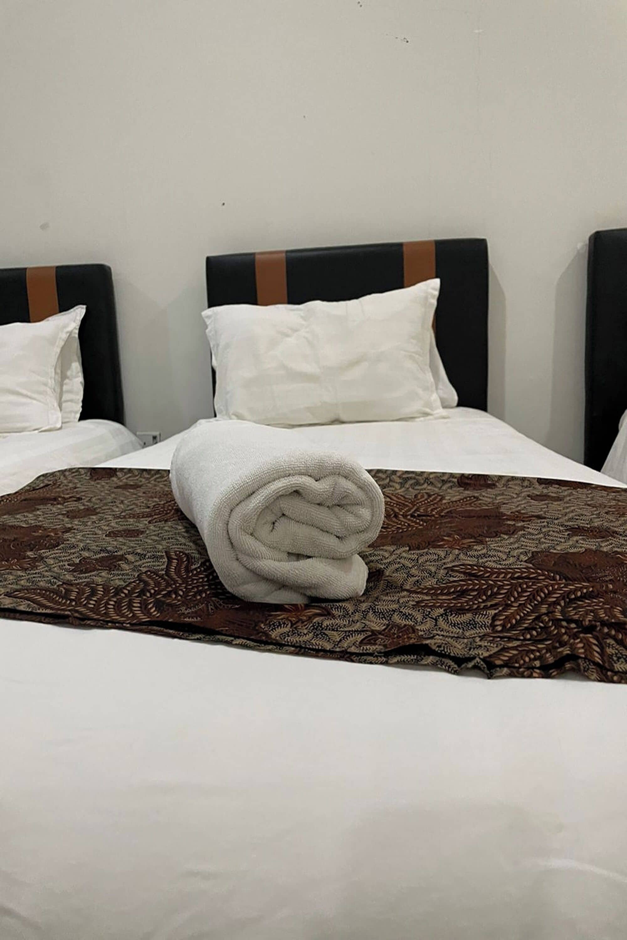 Una cama bien hecha con una colcha estampada y una toalla enrollada encima.