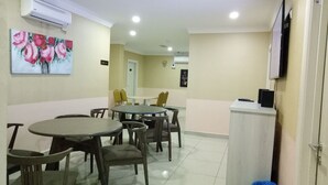 Un comedor con mesas y sillas redondas, un cuadro de flores en la pared y un televisor sobre un mueble.