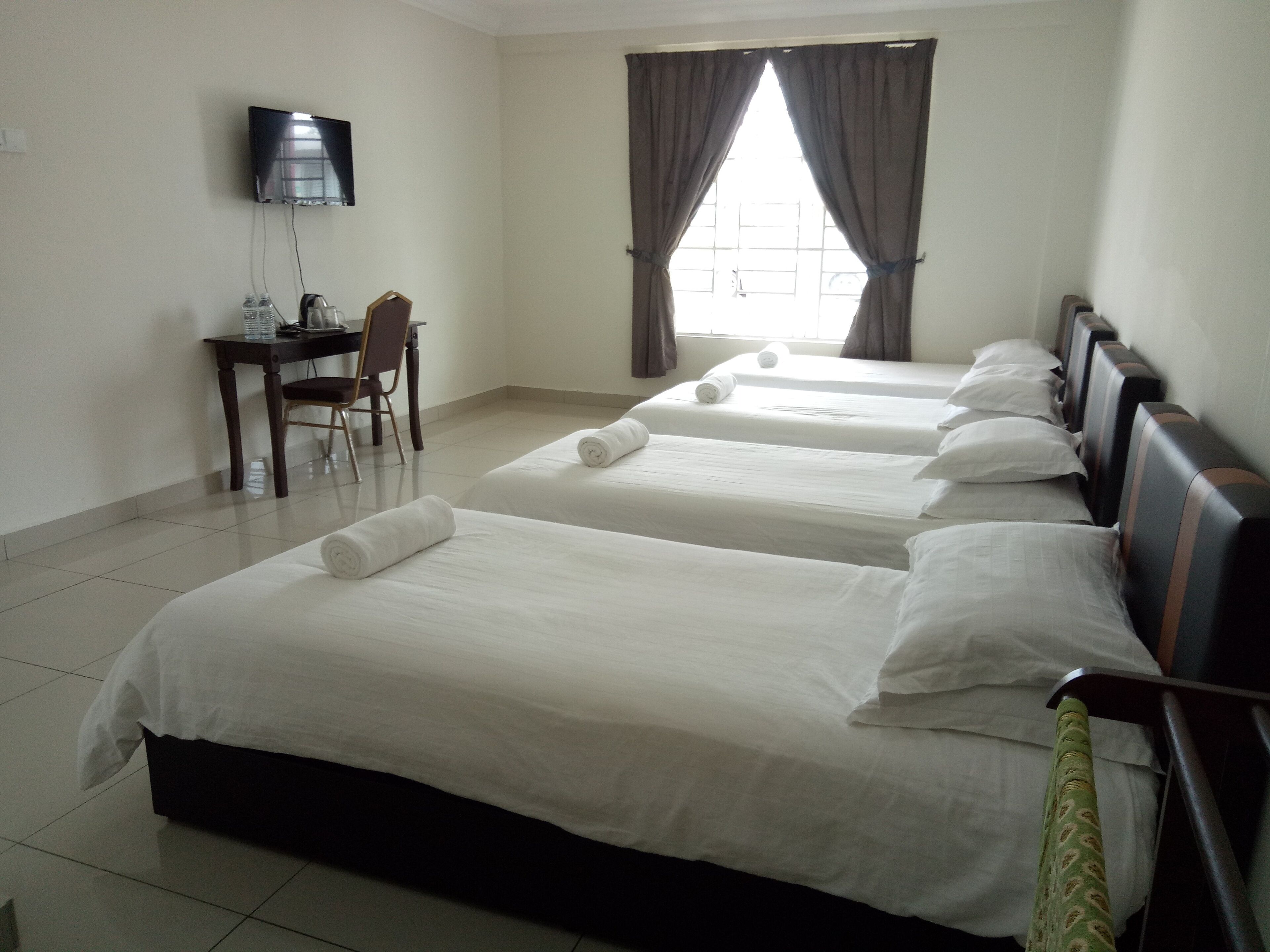 A hotel room with three beds, a desk, a chair, a television, and a window with curtains.