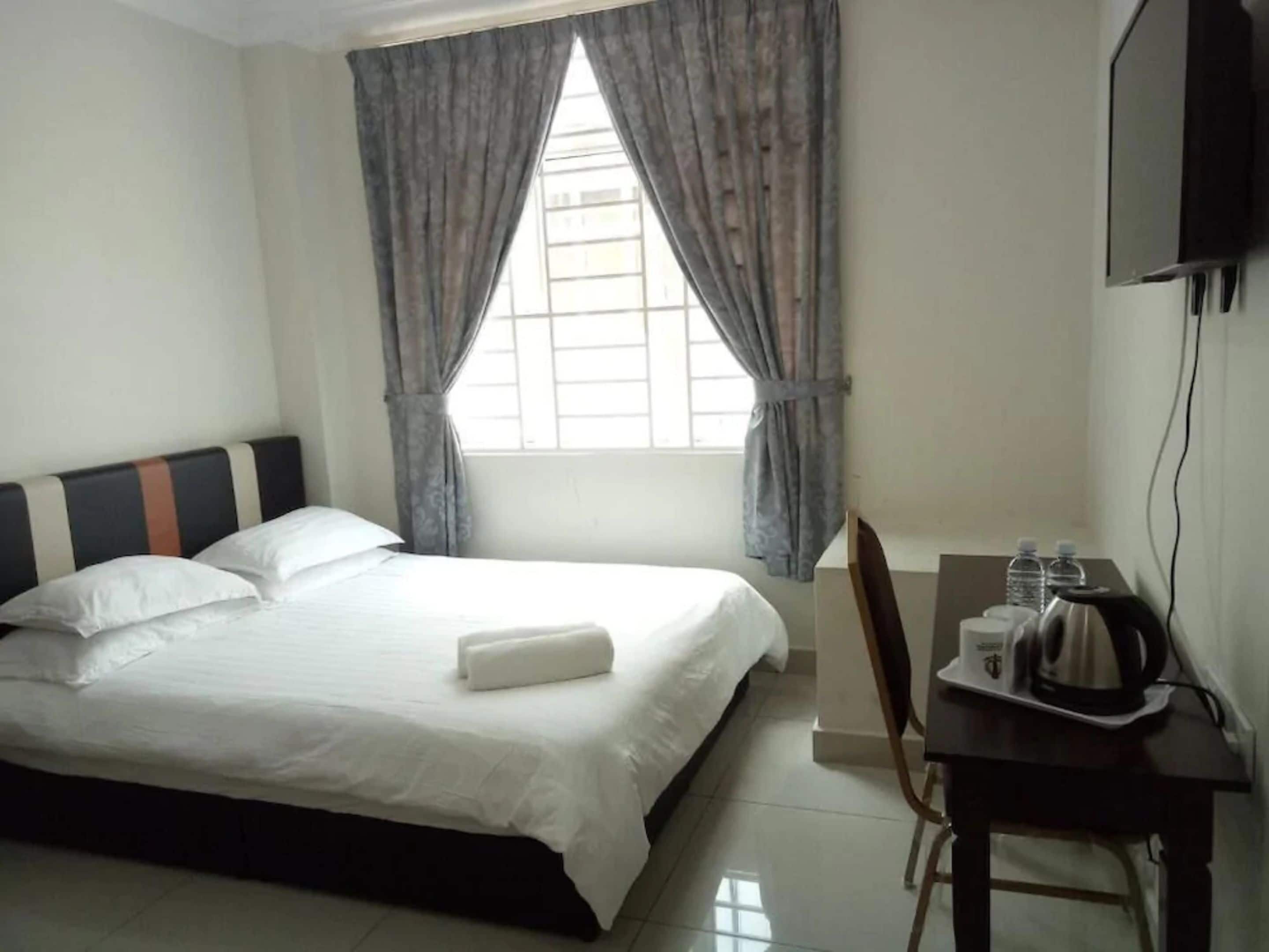 A hotel room with a bed, a desk with a kettle, and a television on the wall.